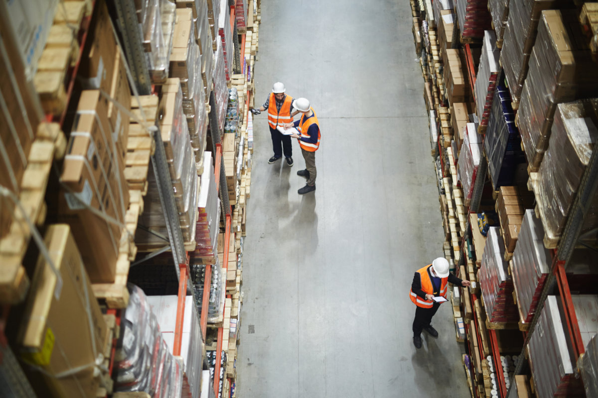 Above view of warehouse workers group in aisle between rows of tall shelves full of packed boxes and goods